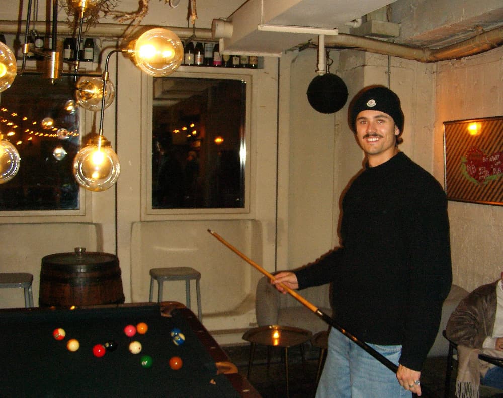 Jack Racovalis smiling, holding a pool cue at a bar